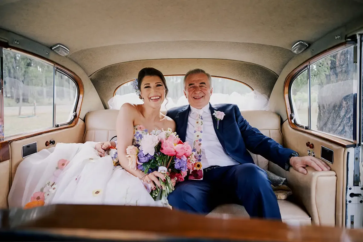 Bride with an elegant updo sitting beside her father in the wedding car